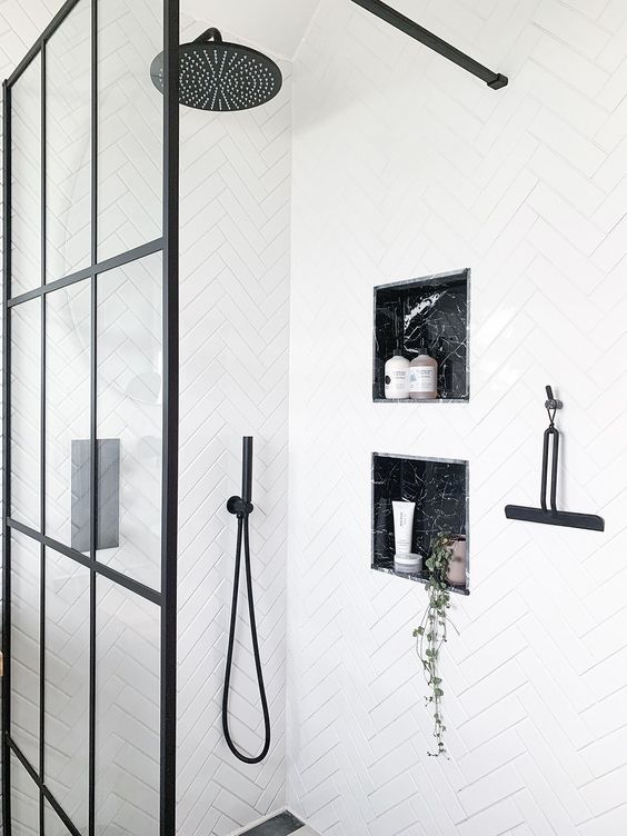 a white bathroom accented with black fixtures and grey marble niches in the shower space