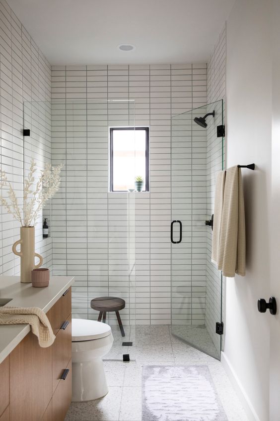 a small and cozy bathroom with skinny tiles, a wooden floating vanity and black fixtures is chic