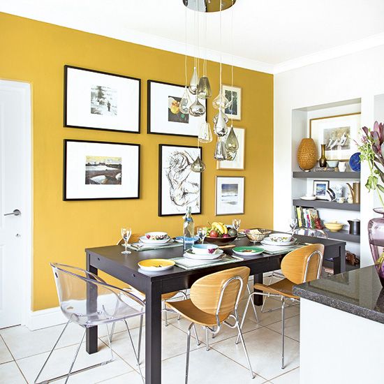 a bold modern dining room with a mustard accent wall, a black table, some pretty chairs, niche shelves and a chic gallery wall