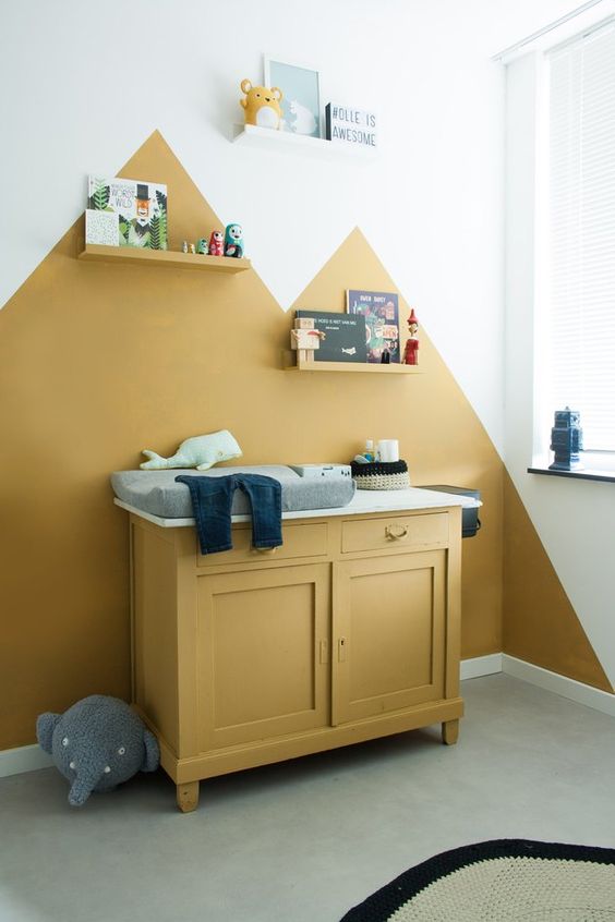 a bold nursery with mustard color blocking on the wall, a mustard cabinet, shelves, toys and artworks and grey touches