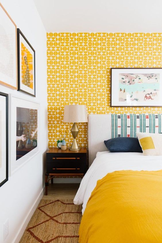 a bright retro bedroom with yellow wallpaper, a bold bed and bedding, a pretty gallery wall and vintage lamps