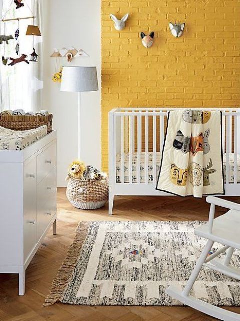a cheerful nursery with a yellow brick wall, white furniture, a printed rug, funny taxidermy and a mobile plus baskets