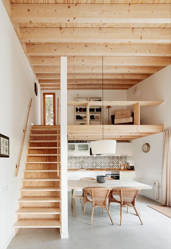 A contemporary home with a wooden ceiling and a staircase, with a kitchen down and a loft reading space with built in shelves
