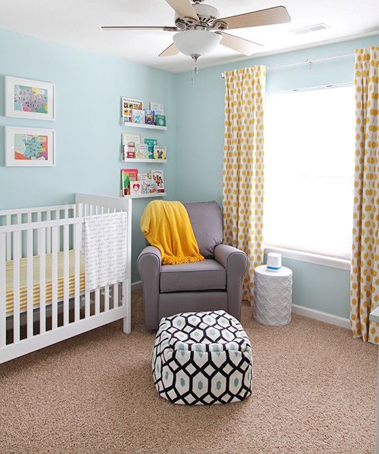 a cozy nursery with light blue walls, a white crib, a grey chair, yellow linens and ledges with books and artworks