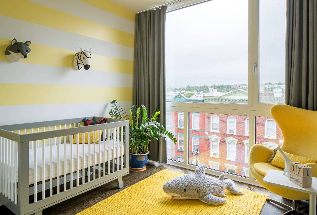 a funny nursery with a striped yellow wall, rug and a chair, grey and white furniture and faux taxidermy