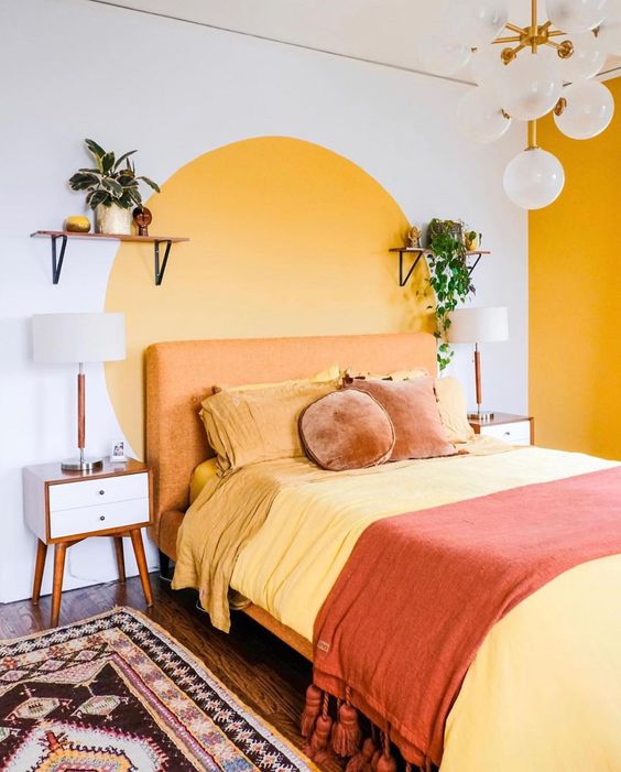 a retro bedroom with a yellow accent wall and a color block one, with an orange bed, pretty nightstands, vintage lamps and a boho rug