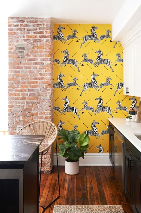 a stylish retro kitchen with black and white cabinetry, a black kitchen island, a brick pillar and yellow zebra wallpaper