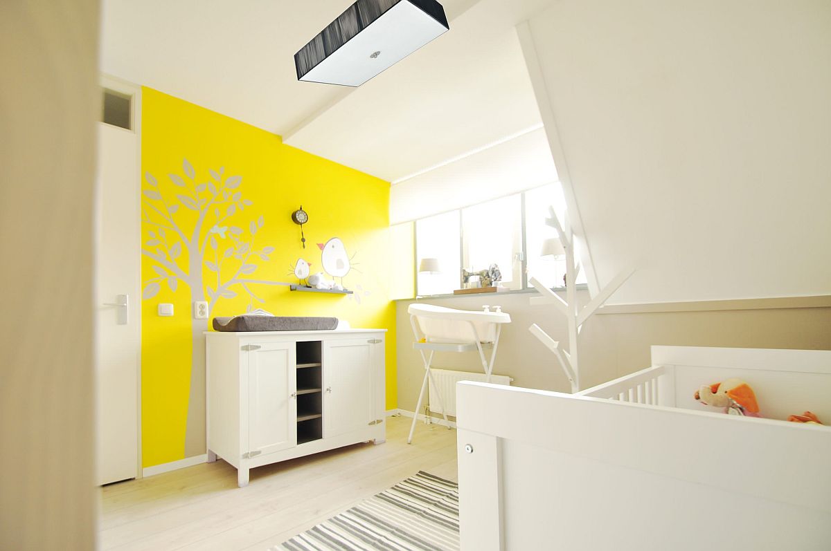 a vivacious yellow and white nursery with a painted accent wall in yellow, wihte furniture, a striped rug and a comfy lamp is wow