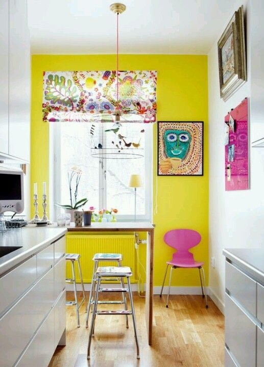 a whimsical kitchen with a shiny yellow wall, bold artworks, a console table and stools, a floral shade on the window