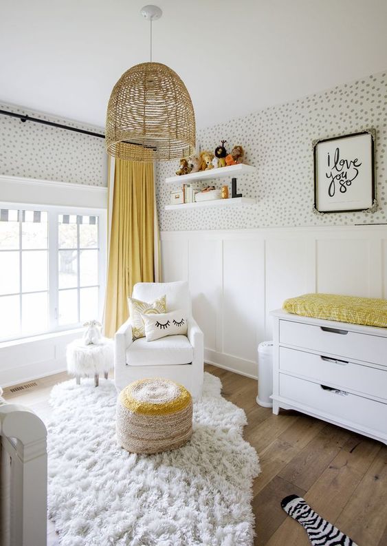 an airy and funny nursery with spot wallpaper, white furniture, a wicker lamp and some yellow touches - linens and an ottoman