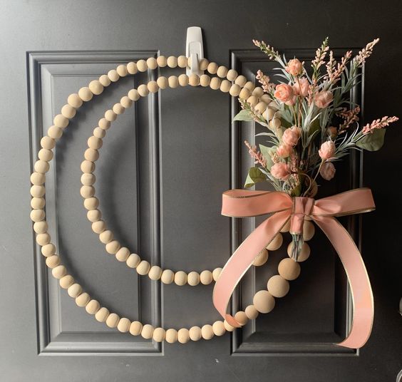 19 a modern boho wreath of wooden beads, with greenery, blush blooms and a pink ribbon bow is a lovely and cool idea