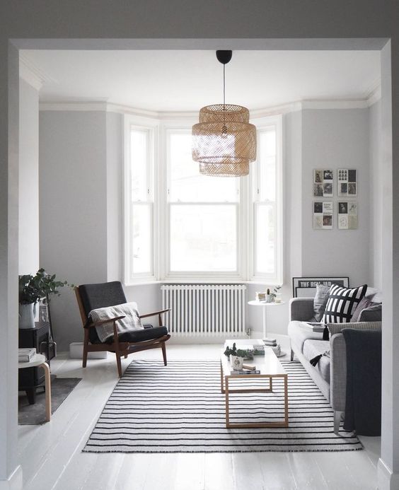 a Nordic living room with a monochromatic color scheme, graphic pillows, a bow window and a woven pendant lamp