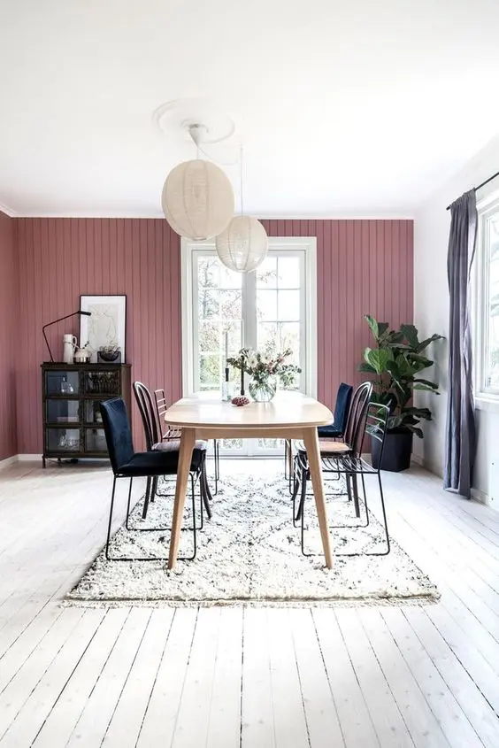 a Scandinavian dining room with a mauve wall, a wooden table, mismatching chairs, paper lamps and a dark buffet