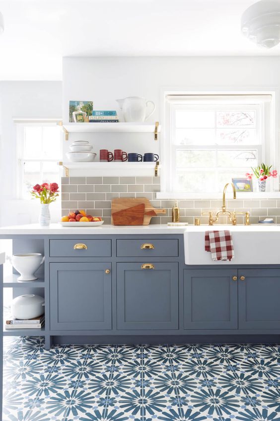 a beautiful blue shaker style kitchen with a grey subway tile backsplash, white quartz countertops and touches of brass