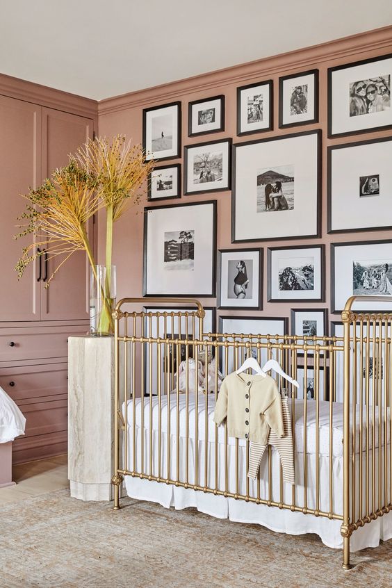 a beautiful mauve nursery with built-in furniture, a gold crib, a monochromatic gallery wall and neutral textiles