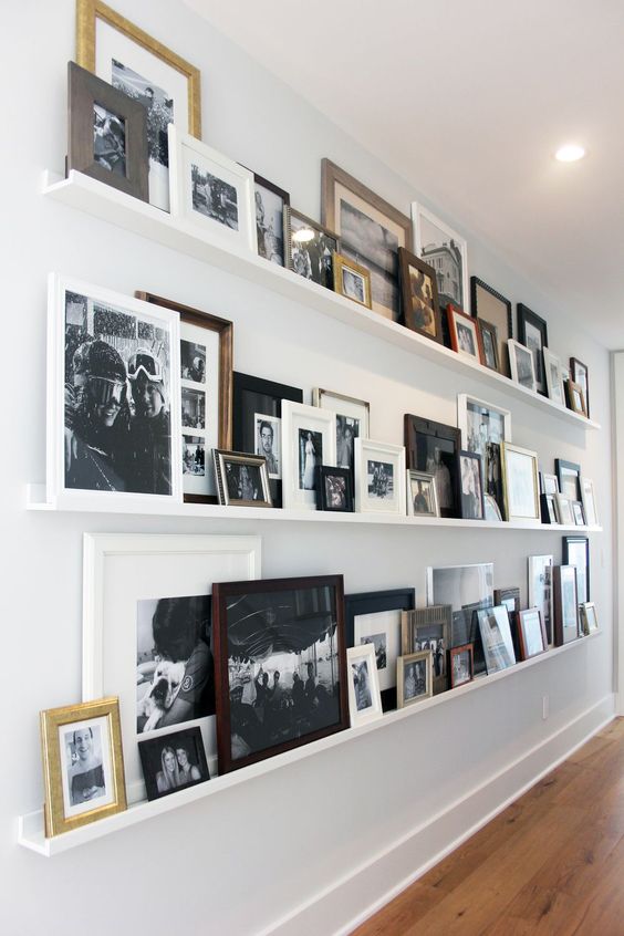 a blank wall int he corridor taken by long white ledges and all kinds of family photos in black and white in mismatching frames adds warmth and coziness to the house