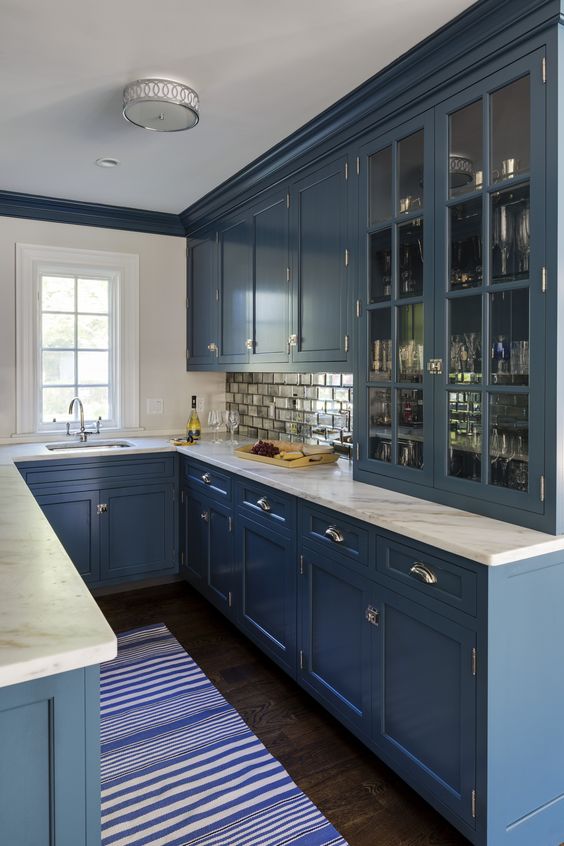 A blue U shaped kitchen with white stone countertops and a mirror tile backsplash is a very stylish space