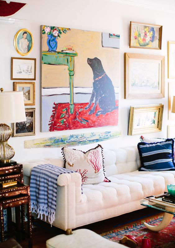 A bright gallery wall with a bold non framed artwork in the center and some mismatching artworks around