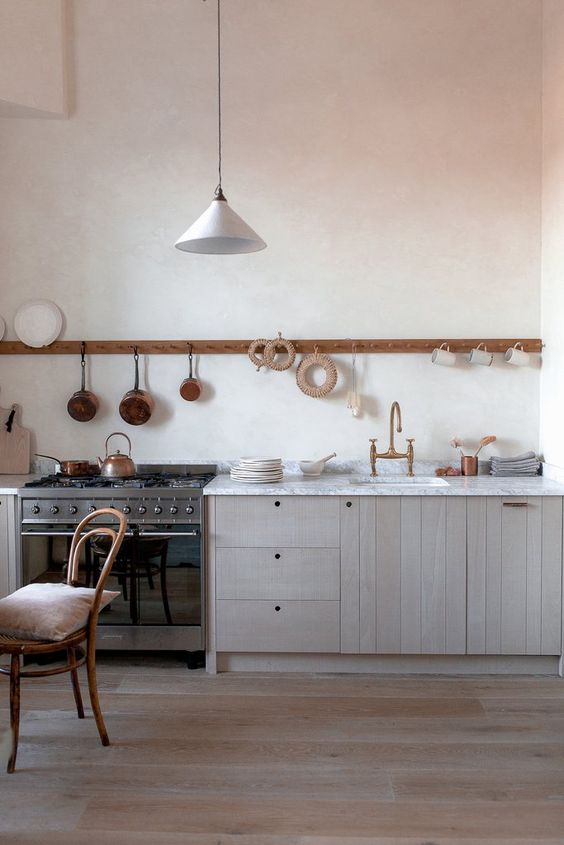a chic blonde wood one wall kitchen with a white stone countertop and a long holder with mugs and pans
