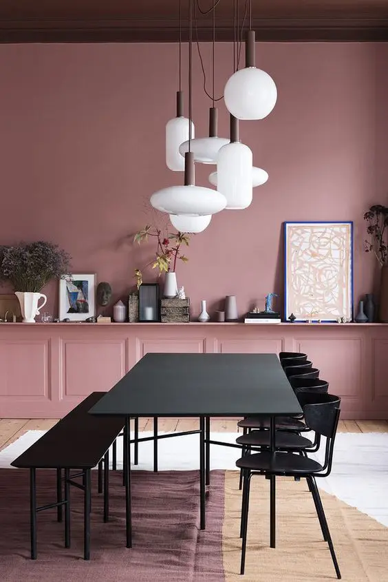 a chic mauve dining room with black furniture and a long shelf showing off various vases and decor plus a cluster of pendant lamps
