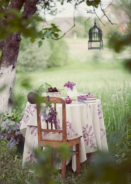 a chic rustic dining area with a table and a chair placed under the tree, a candle lantern and a pretty floral tablecloth