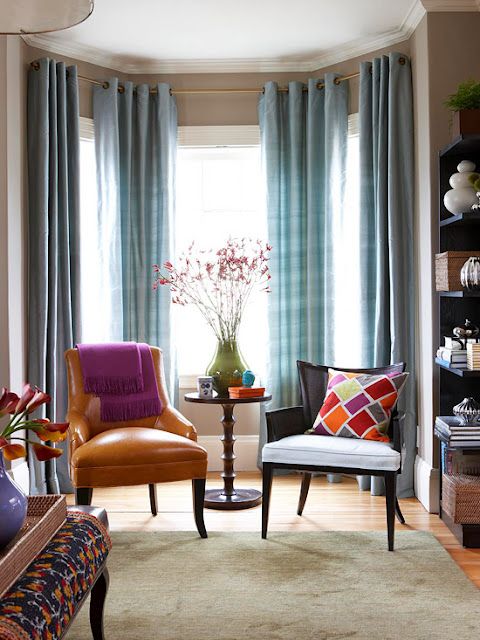 a colorful nook with a bow window, blue plaid curtains, colorful chairs and pillows plus a round table