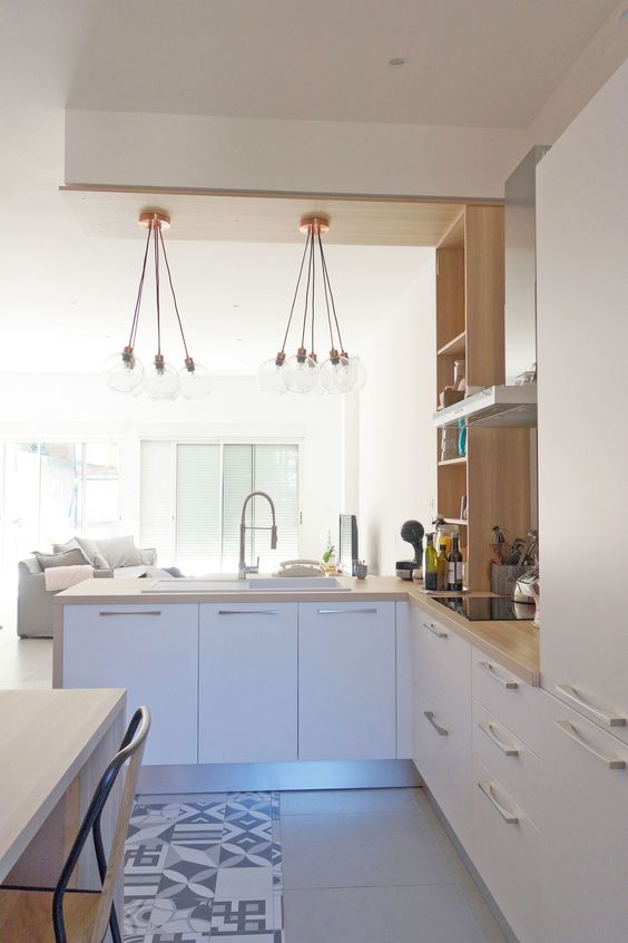 A contemporary white L shaped kitchen with butcherblock countertops and wooden shelves, with pendant lamps