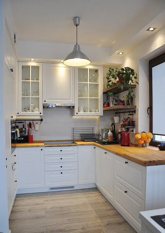 A cool U shaped kitchen in white, with glass cabinets, a pendant lamp and butcherblock countertops