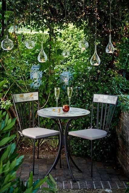 a cool garden eating space with hanging candleholders, a round table and chairs looks welcoming and cool