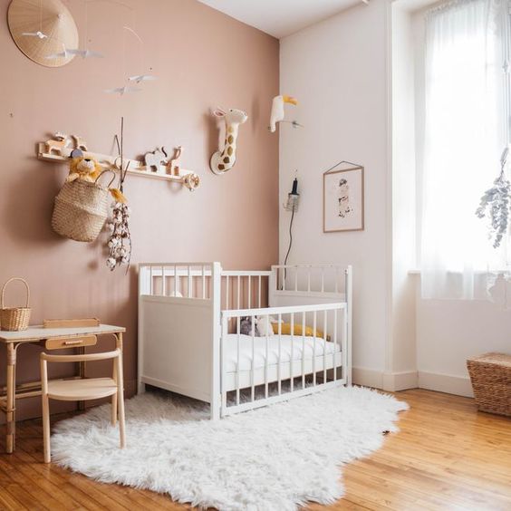 a cool nursery with a mauve accent wall, neutral and white furniture, a gallery wall and a shelf over the space