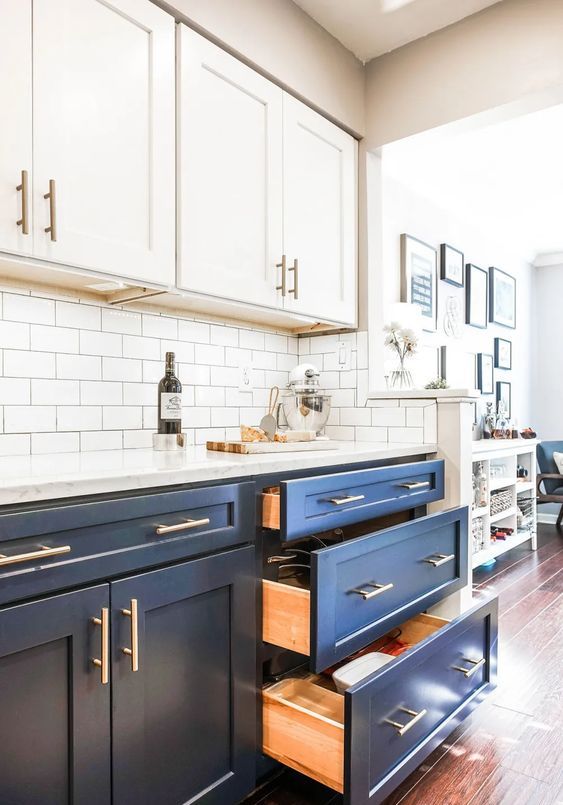 a cool two tone kitchen with navy and white shaker style cabinets, white quartz countertops and a white subway tile backsplash