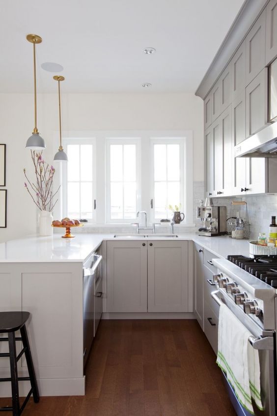 A cozy grey U shaped kitchen with white stone countertops, a white marble tile backsplash and elegant lamps