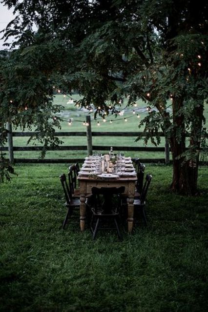 a cozy little dining area with a wooden table, black chairs and lights over it hanging from the tree
