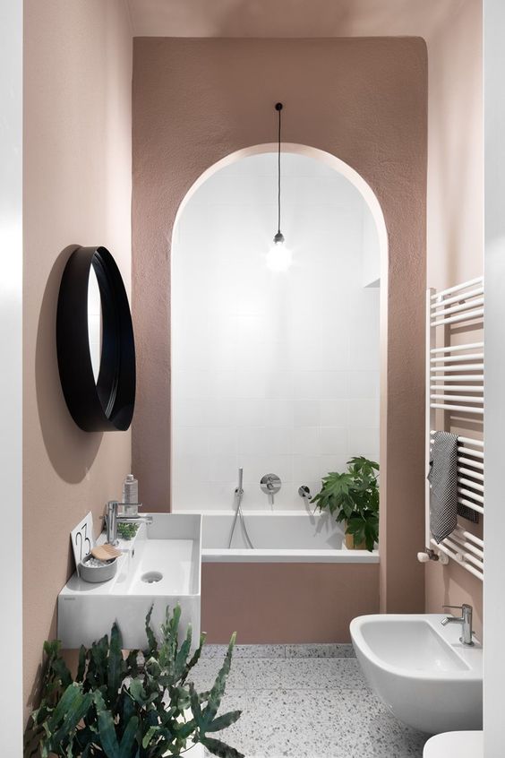 A creative mauve bathroom with an archway to the bathtub, a free standing sink, a round mirror and plants