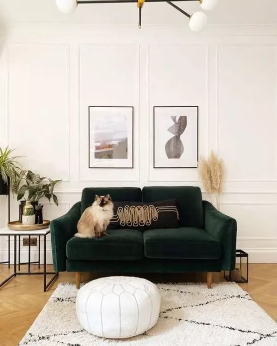 a cute living room done in neutrals, with a dark green sofa, a white leather pouf, a side table, a mini gallery wall