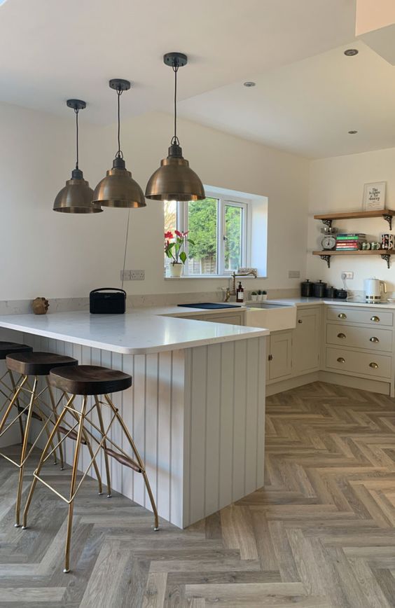 A dove grey U shaped kitchen with white countertops, open shelves, metal pendant lamps and cool stools