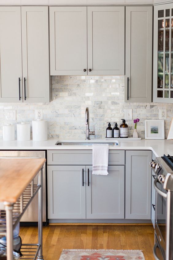 a dove grey shaker style kitchen with a white marble tile backsplash and white countertops plus black fixtures is chic