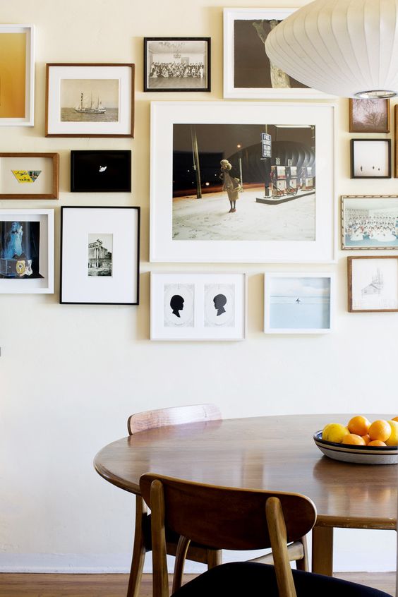 a free form gallery wall with thin black, white and wooden frames and white matting but mismatching black and white and color art