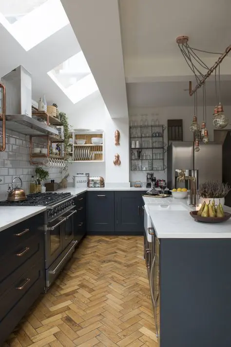 a graphite grey kitchen with white countertops, skylights, brass fixtures and hanging bulbs