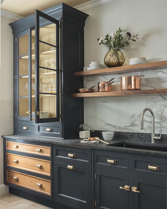 a graphite grey vintage kitchen with gold handles, a black stone countertop and a white stone backsplash