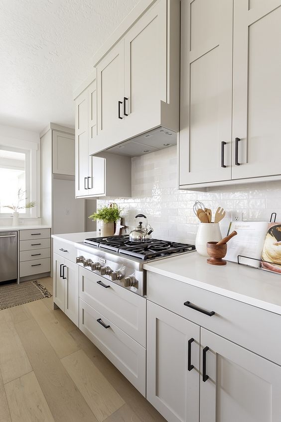a grey farmhosue kitchen with shaker style cabinets, a white tile backsplash and white countertops plus black fixtures