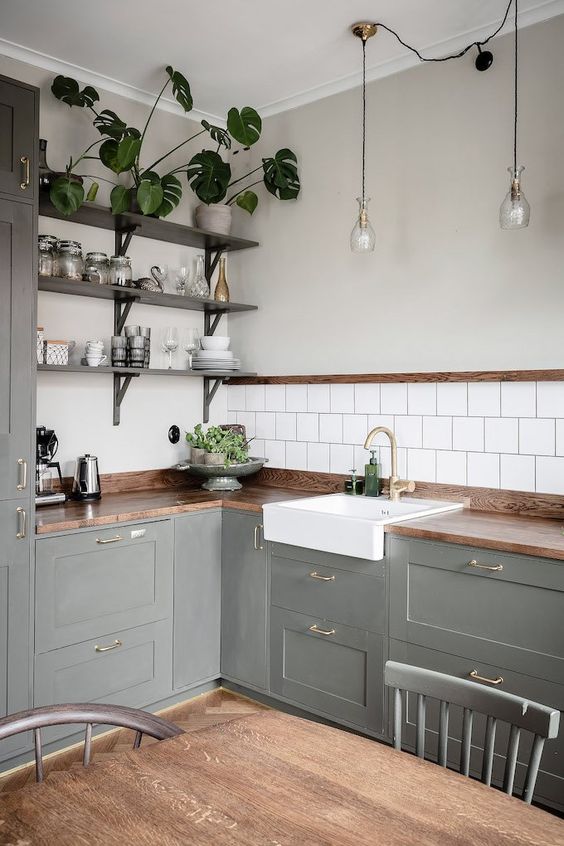 A grey rustic L shaped kitchen with butcherblock countertops, open shelves and potted greenery plus pendant lamps