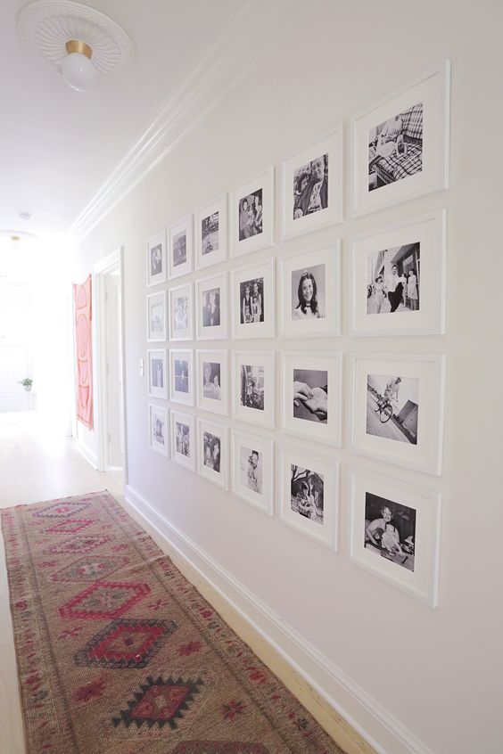 a large symmetrical gallery wall with matching white frames and black and white pictures of the family accents the long corridor