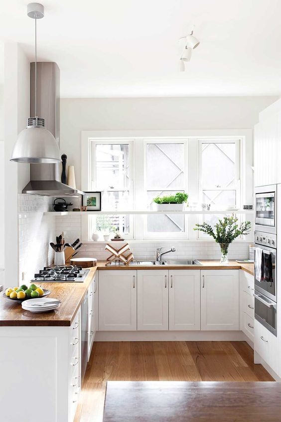 a light-filled white U-shaped kitchen with butcherblock countertops, a white pendant lamp and greenery