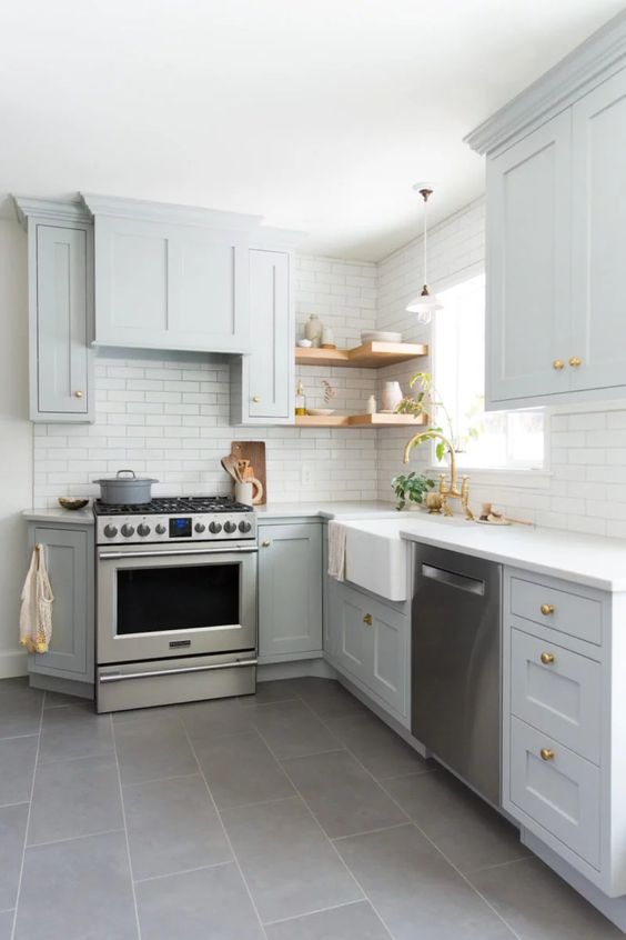 A light grey L shaped kitchen with open shelves, a white tile backsplash and gold handles is a very stylish and cozy space