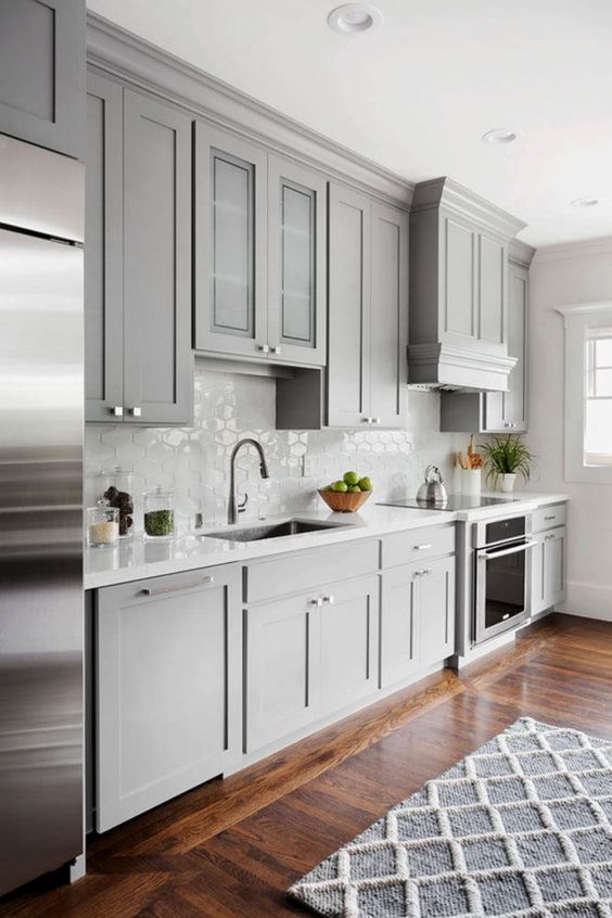 a light grey kitchen with shaker cabinets, a white Moroccan tile backsplash and white coutnertops plus stainless steel touches