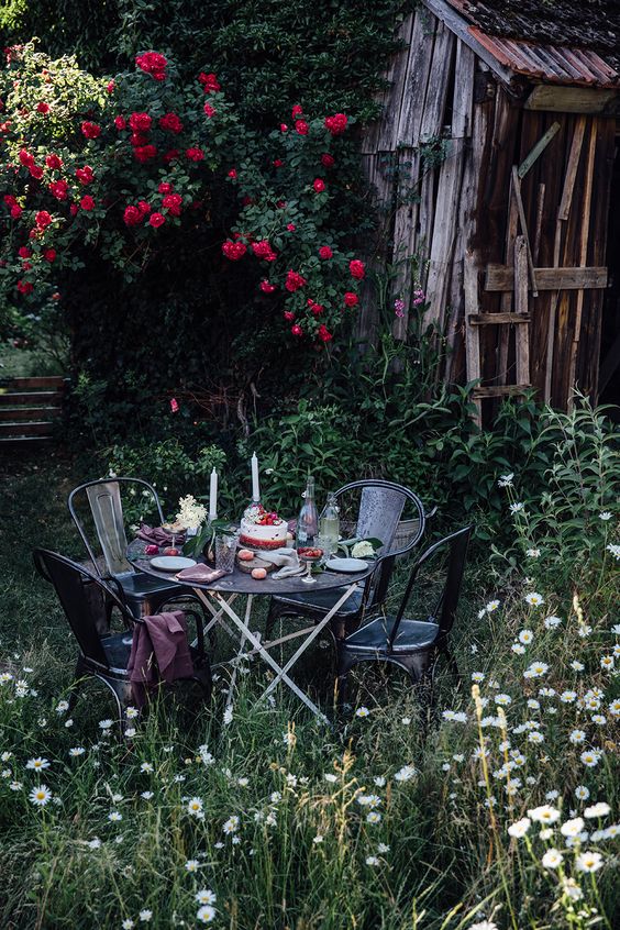 a little garden eating nook with a metal table and some meatching chairs plus blankets created in blooming surroundings