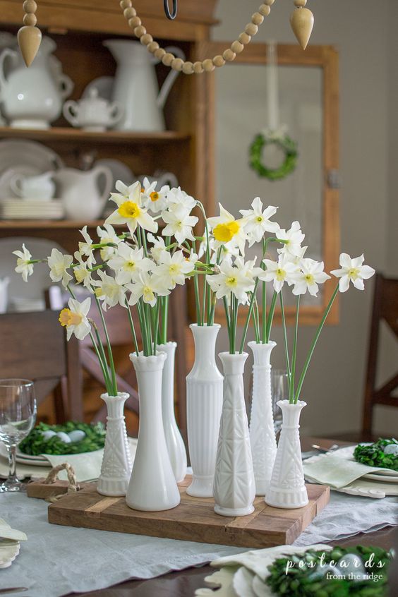 a lovely and simple spring cluster centerpiece of mismatching vases with daffodils placed on a wooden board