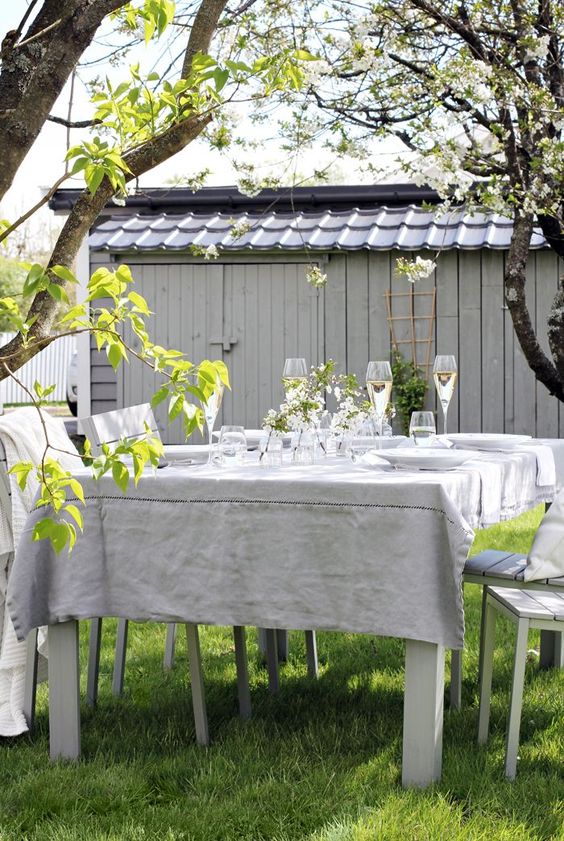 a lovely backyard dining space with a table and chairs under the trees, with blooms on the table