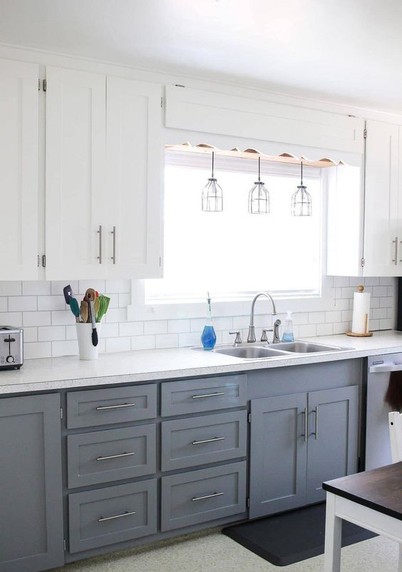 a lovely two tone kitchen with grey and white shaker cabinets, a white subway tile backsplash and white countertops plus industrial pendant lamps